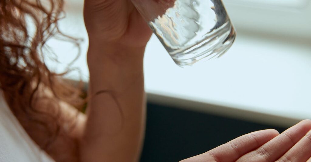 Close-up of a woman holding pills and a glass of water indoors.